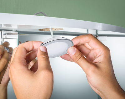 Mains installant un spot LED encastré rond blanc en plastique dans un meuble avec fond vert