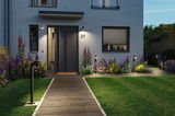 Modern entrance with black outdoor lights and well-kept garden featuring colorful flowers.