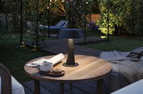 Black metal outdoor table lamp on wooden table with coffee and cookies in garden at dusk