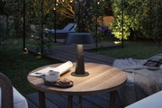 Black metal outdoor table lamp on wooden table with coffee and cookies in garden at dusk
