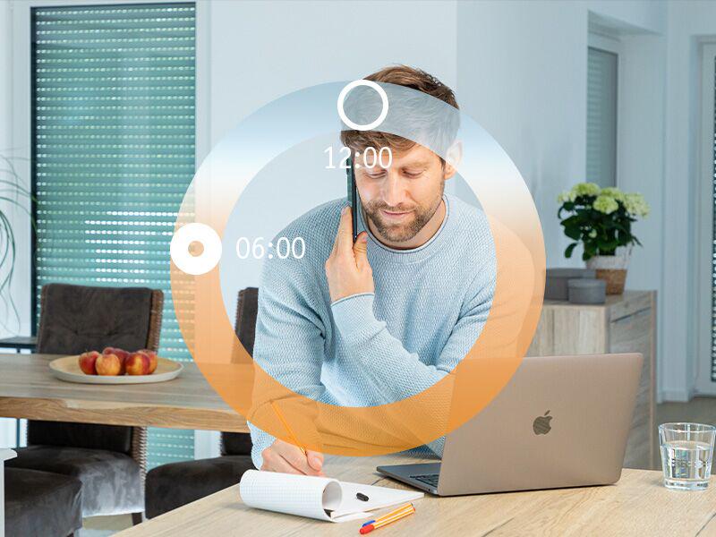Mann am Schreibtisch mit Laptop und Notizblock, Tageslichtzyklus-Visualisierung über dem Bild.