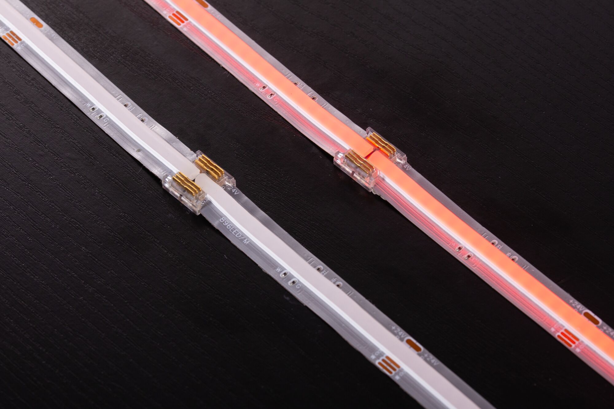 Two LED light strips in white and red with transparent connectors on black surface, LED lighting detail.
