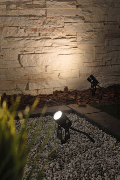 Black LED outdoor spotlight on gravel with warm white light, perfect for garden and wall lighting
