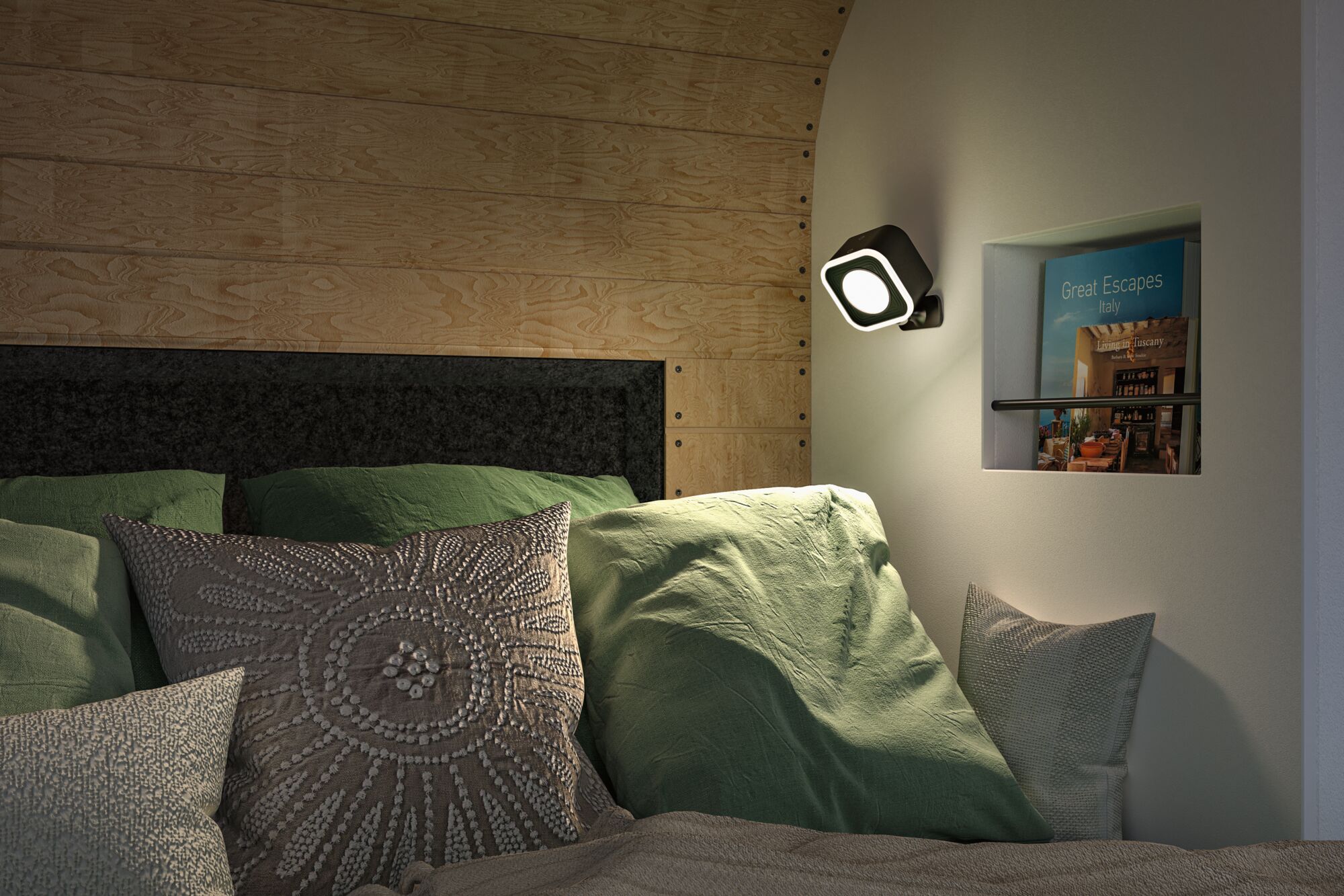 Black square LED wall light mounted in bedroom with green pillows and wooden wall paneling, modern lighting.
