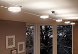 Moderne witte LED-kabelverlichting met ronde armaturen in woonkamer met grote ramen en wanddecoratie.