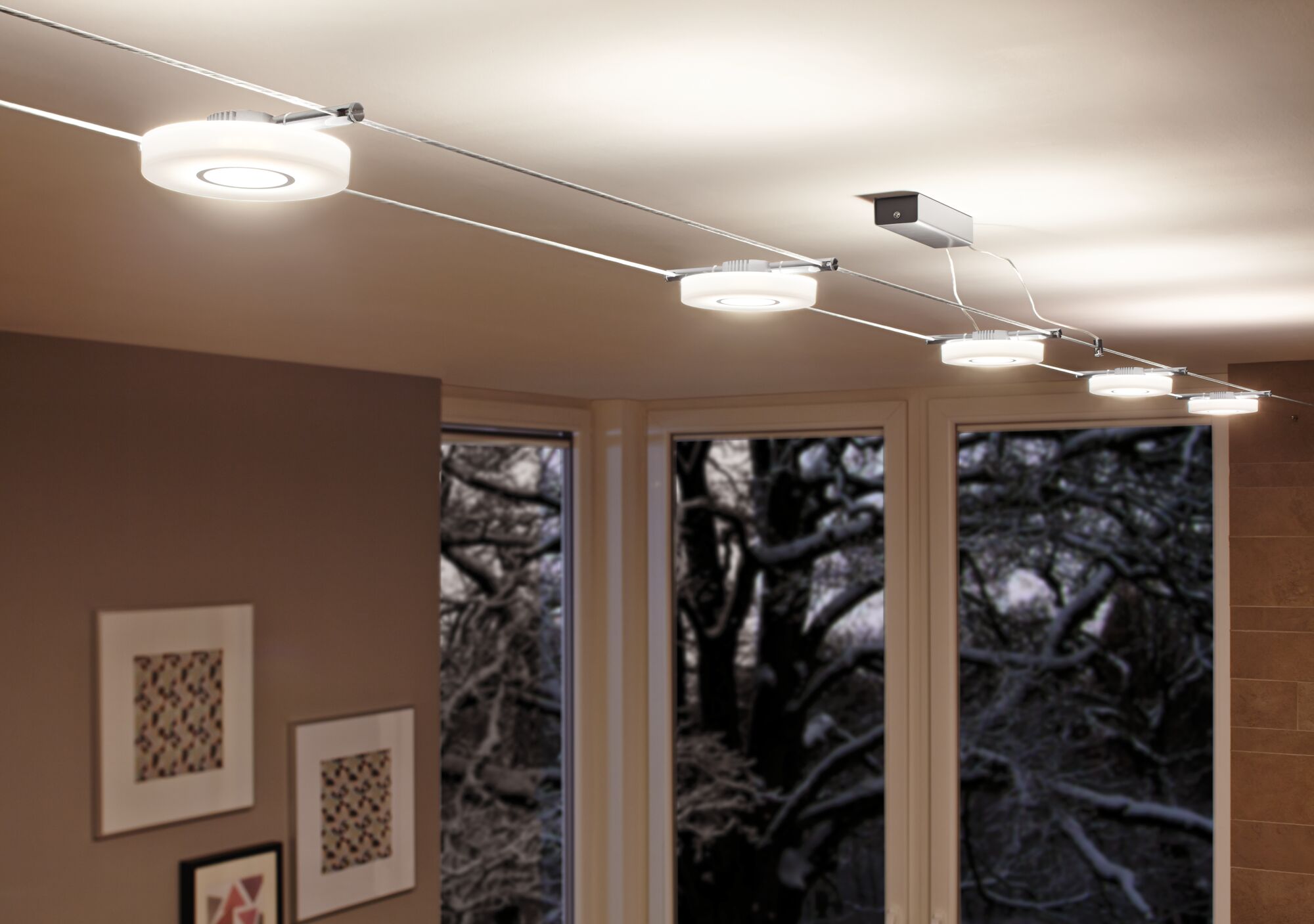 Moderne weiße LED-Seilbeleuchtung mit runden Leuchten in Wohnraum mit großen Fenstern und Kunst an der Wand.