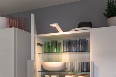 Hvid LED-skabslygte lyser glas og skåle på glashylder i moderne køkkenskab