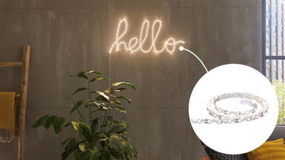 Warm white LED string lights shaped as hello text on grey wall with indoor plant in modern room