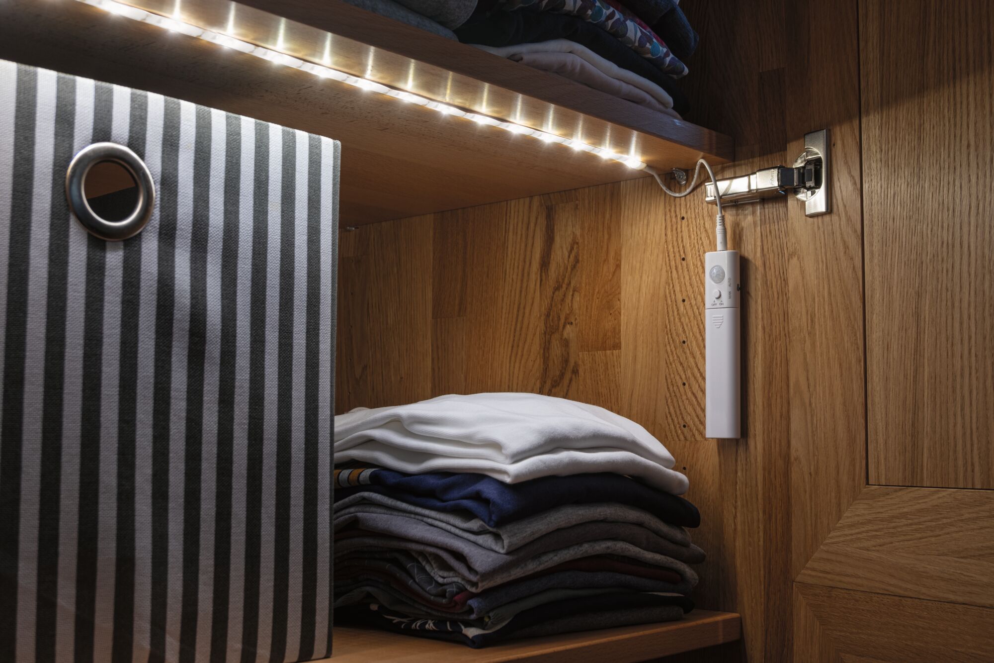 Bande LED avec détecteur de mouvement dans armoire en bois éclairant vêtements pliés et boîte de rangement