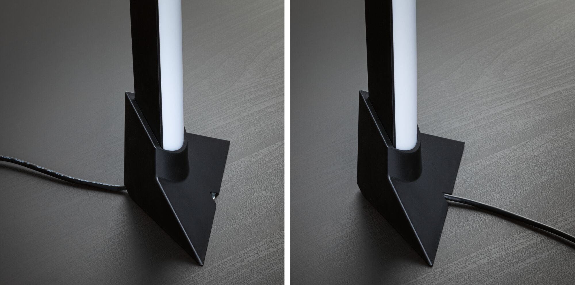 Zwarte metalen lamp met witte lichtbuis en kabel op grijze houten vloer, modern ontwerp.