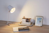 Witte bureaulamp met metalen voet verlicht houten bureau met marmeren organizer en blauwe fotolijst.