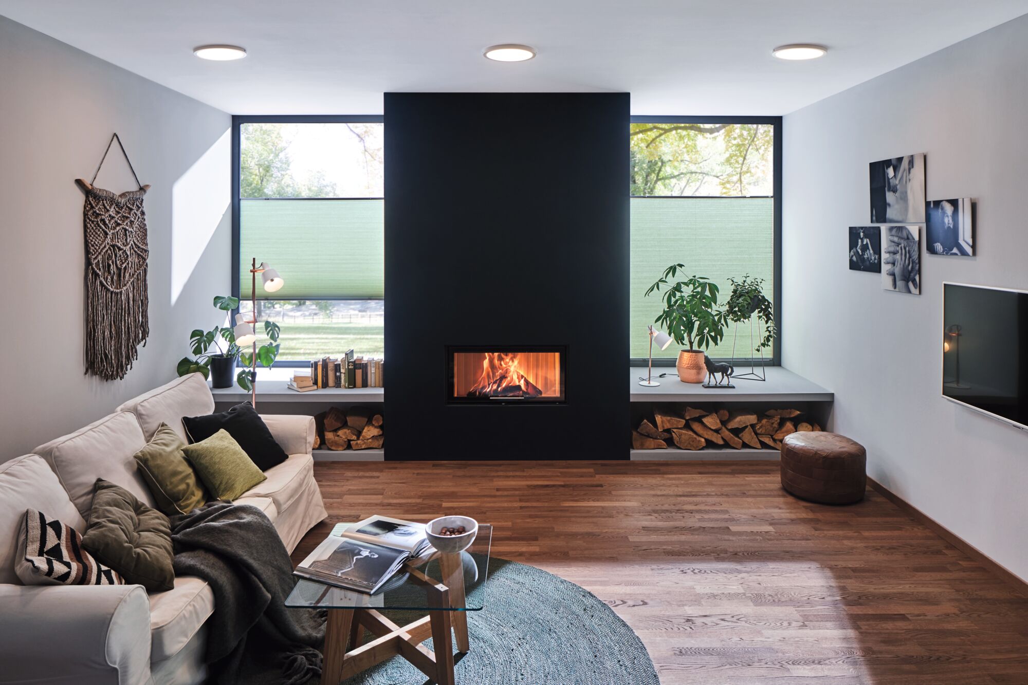 Moderne woonkamer met witte bank, houten vloer, open haard en ronde plafondlampen met warm wit licht.