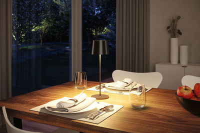 Modern black metal table lamp on wooden dining table with set plates and apples