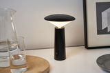 Modern black LED table lamp with conical lampshade on white table next to glass of water