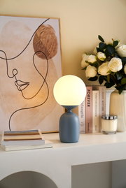 Modern grey table lamp with round white glass shade and decorative abstract art in background