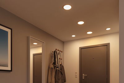 Warm LED recessed lights in hallway with brown door and wooden metal coat rack.