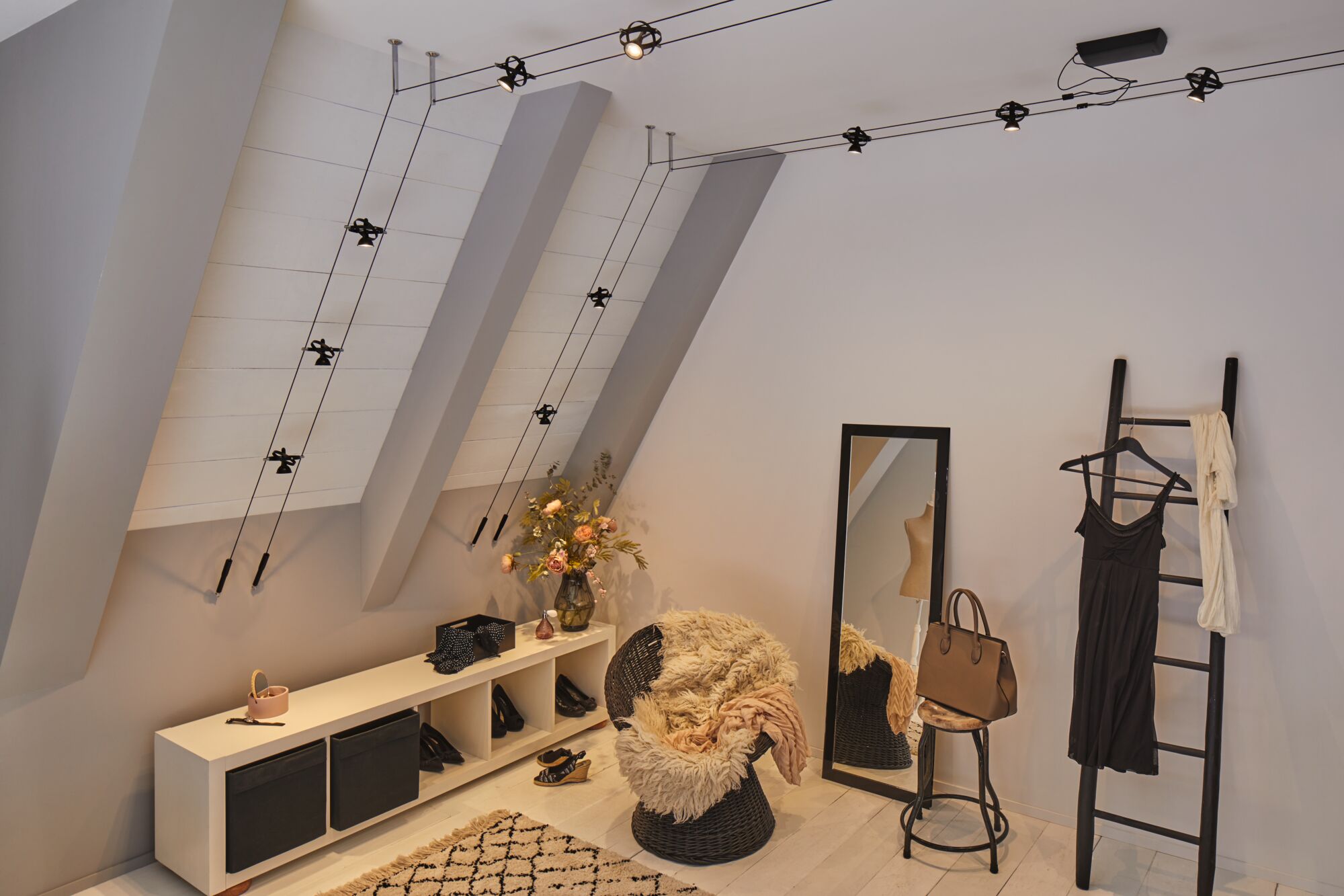 Modern room with black cable-pulled ceiling light, mirror, wicker chair, and warm decorative accents