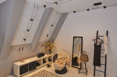 Chambre moderne avec suspension noire à câble, miroir, fauteuil en osier et décorations chaleureuses