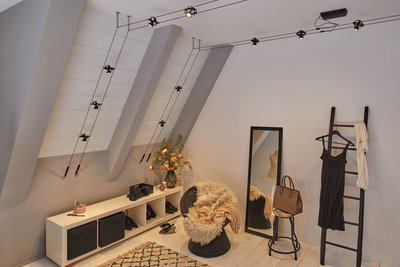 Modern room with black cable-pulled ceiling light, mirror, wicker chair, and warm decorative accents