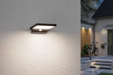 Black LED outdoor wall light with motion sensor mounted on white wall illuminating entrance area.