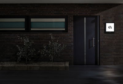 Porte d'entrée moderne gris foncé avec poignée en acier inoxydable et panneau lumineux de numéro de maison.