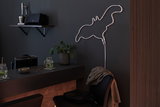 Lampe néon LED blanche en forme de flamant sur mur sombre dans un espace moderne avec bar et plante