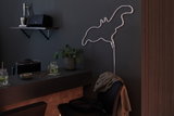 Lampe néon LED blanche en forme de flamant sur mur sombre dans un espace moderne avec bar et plante
