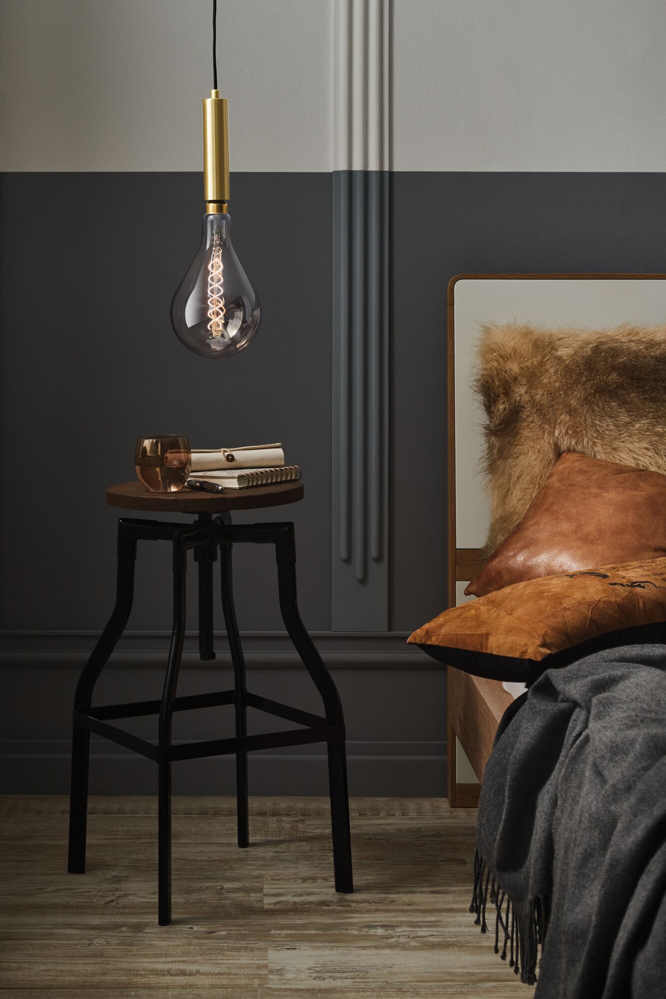 Hanging LED bulb with smoked glass and gold socket above bedside table with notebook and glass