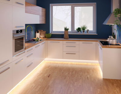 Moderne weiße Küche mit Holzarbeitsplatten und LED-Bodenbeleuchtung für stilvolles Küchendesign.
