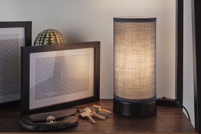Table lamp with grey fabric shade and black base on wooden table next to keys and picture frames