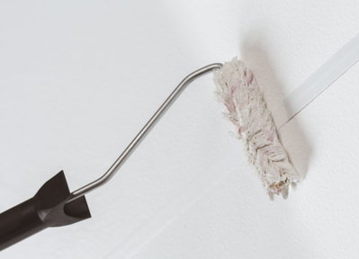 Paint roller with black handle applying white textured paint on wall for painting tools