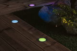 Farvede LED-indbygningsgulvlamper i rustfrit stål på træterrasse ved have med sten og planter