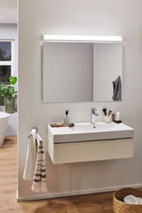 Modernes Badezimmer mit weißem Wandwaschbecken, großem Spiegel und LED-Spiegelleuchte für Badbeleuchtung