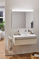 Modernes Badezimmer mit weißem Wandwaschbecken, großem Spiegel und LED-Spiegelleuchte für Badbeleuchtung