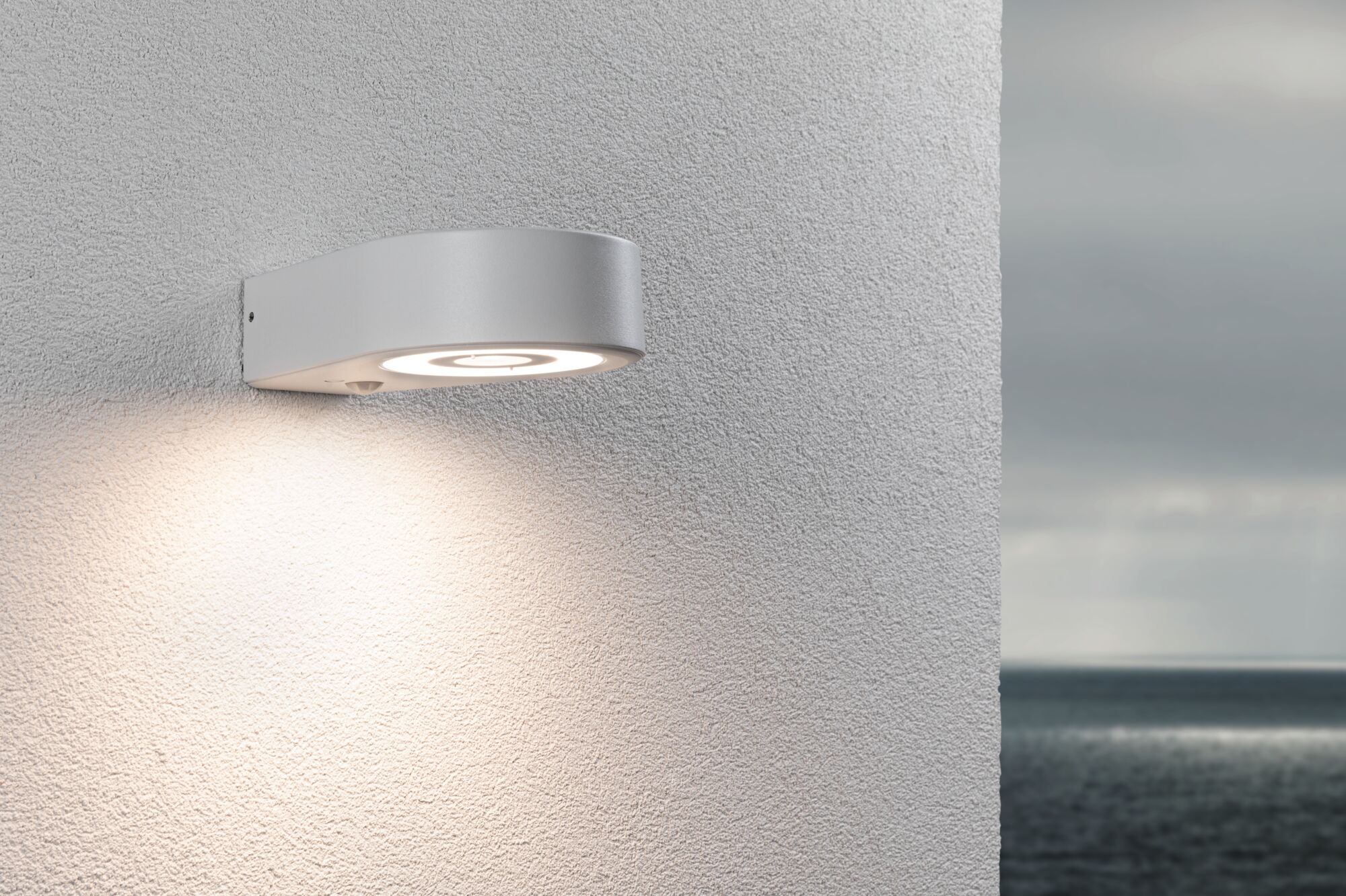 Runde weiße Außenwandleuchte aus Metall mit warmweißem LED-Licht an strukturierter Wand.