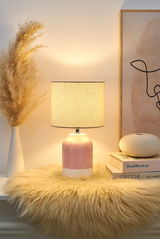 Pink ceramic table lamp with beige fabric shade on fluffy rug beside decor and books