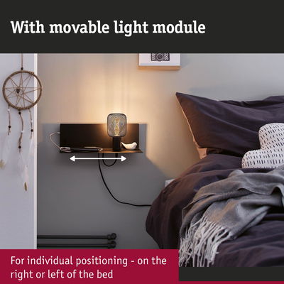 Black wall shelf with movable light module beside bed with dark bedding and dreamcatcher