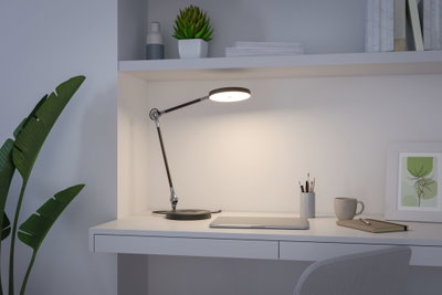 Moderne schwarze LED-Schreibtischlampe mit rundem Leuchtkopf auf weißem Arbeitsplatz mit Laptop und Tasse