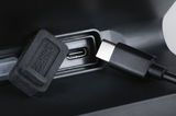 Close-up of black USB-C charging port with protective cap and cable on electronic device.