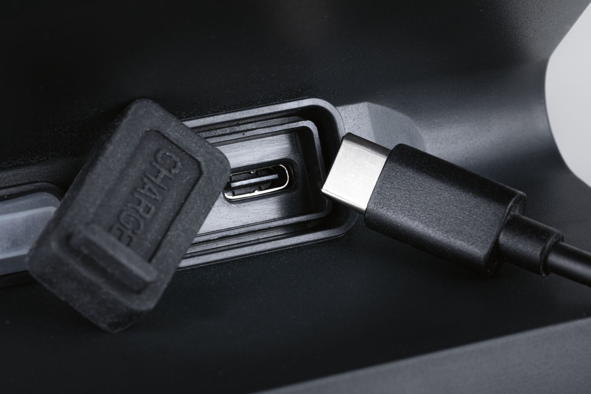 Nahaufnahme eines schwarzen USB-C-Ladeanschlusses mit Schutzkappe und Kabel an einem elektronischen Gerät.