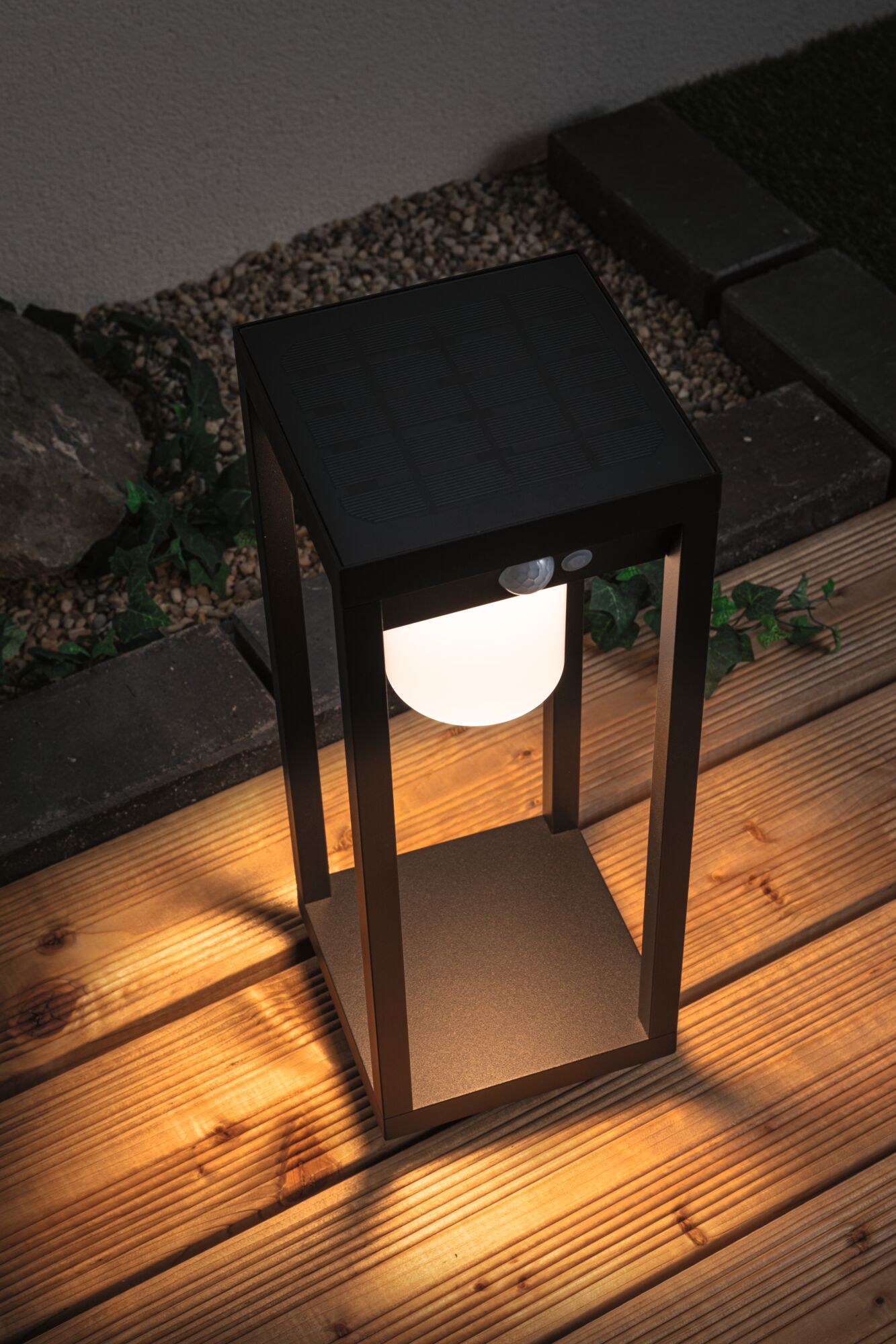 Zwarte metalen solar-lantaarn met warm wit LED-licht op houten terras voor tuinverlichting