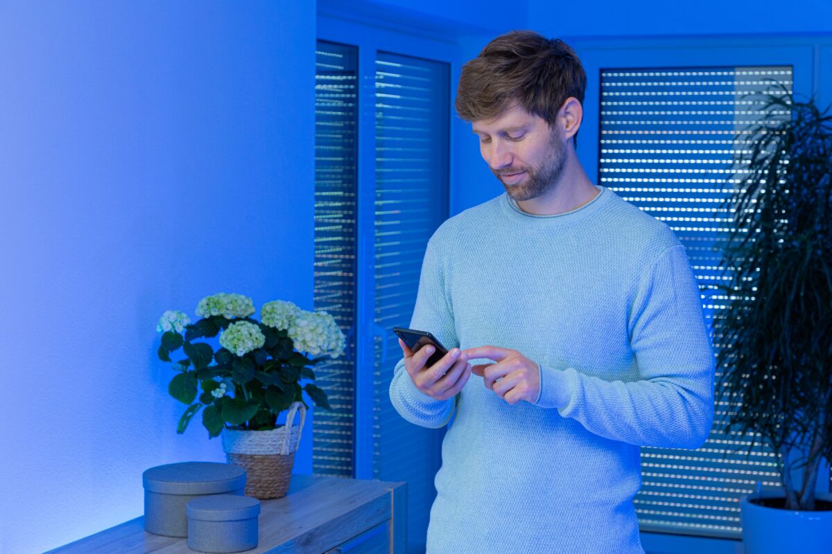 Man in blauwe trui bedient smartphone in moderne kamer met blauwe LED-verlichting en planten