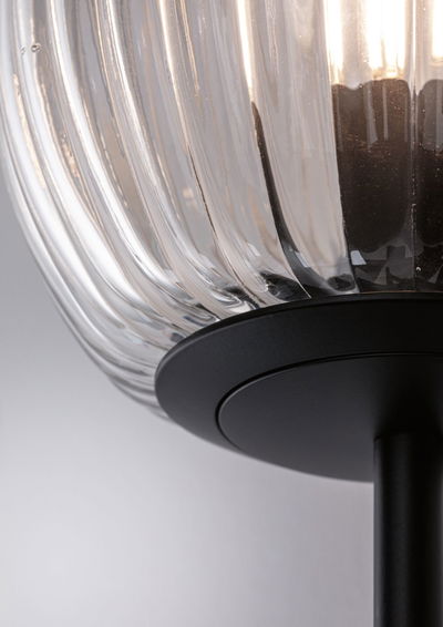 Close-up of clear ribbed glass lamp with black metal base for modern indoor lighting