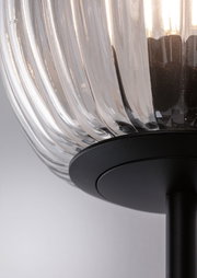 Gros plan d'une lampe en verre cannelé transparent avec base en métal noir pour éclairage intérieur moderne