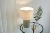Table lamp with grey ceramic base and white fabric shade on glass side table with decor