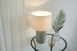 Table lamp with grey ceramic base and white fabric shade on glass side table with decor