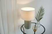 Table lamp with grey ceramic base and white fabric shade on glass side table with decor
