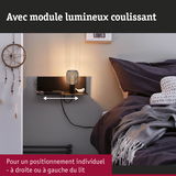 Étagère murale noire avec module lumineux coulissant à côté d'un lit avec literie foncée