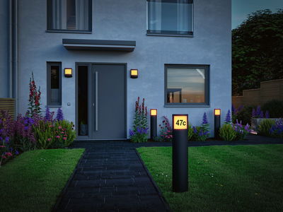 Modern outdoor lighting with black bollard lights and wall lamps on gray house with garden path
