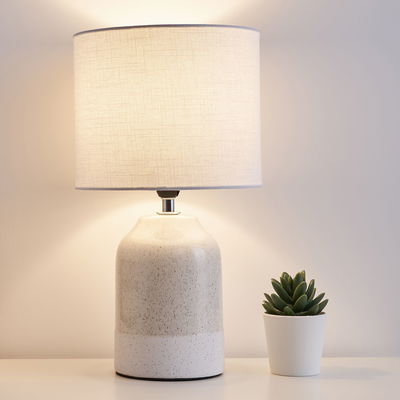 Cream ceramic table lamp with white fabric shade and decorative succulent pot beside it